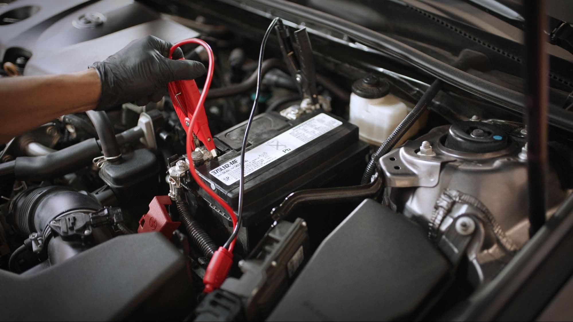 A technician working on a car's 12V battery